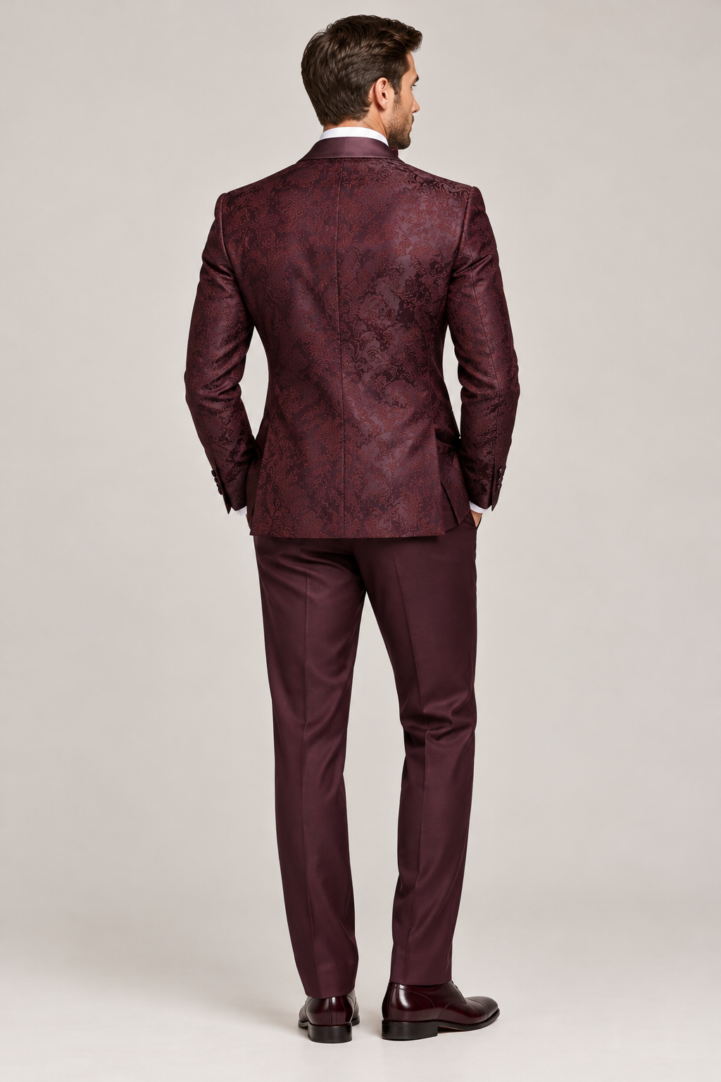 Back view of a model wearing a burgundy patterned tuxedo jacket with matching trousers.