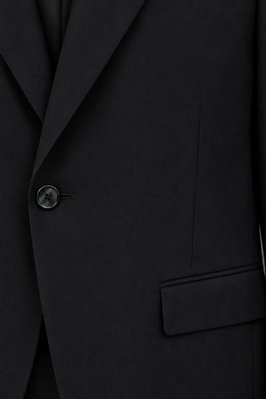 Close-up of plain black suit fabric beside a dark front button and flap pocket seam.