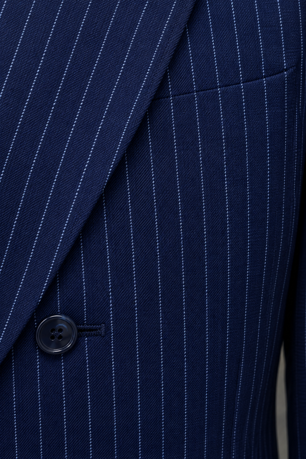 Close-up of fine light pinstripes on navy suit fabric beside a jacket seam and dark button.